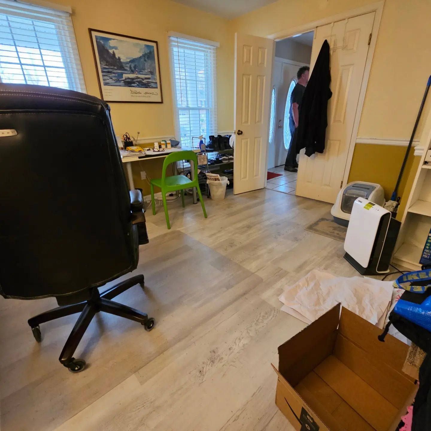 Home office with desk chairs, windows, a coat on the wall, and a person standing in the doorway.