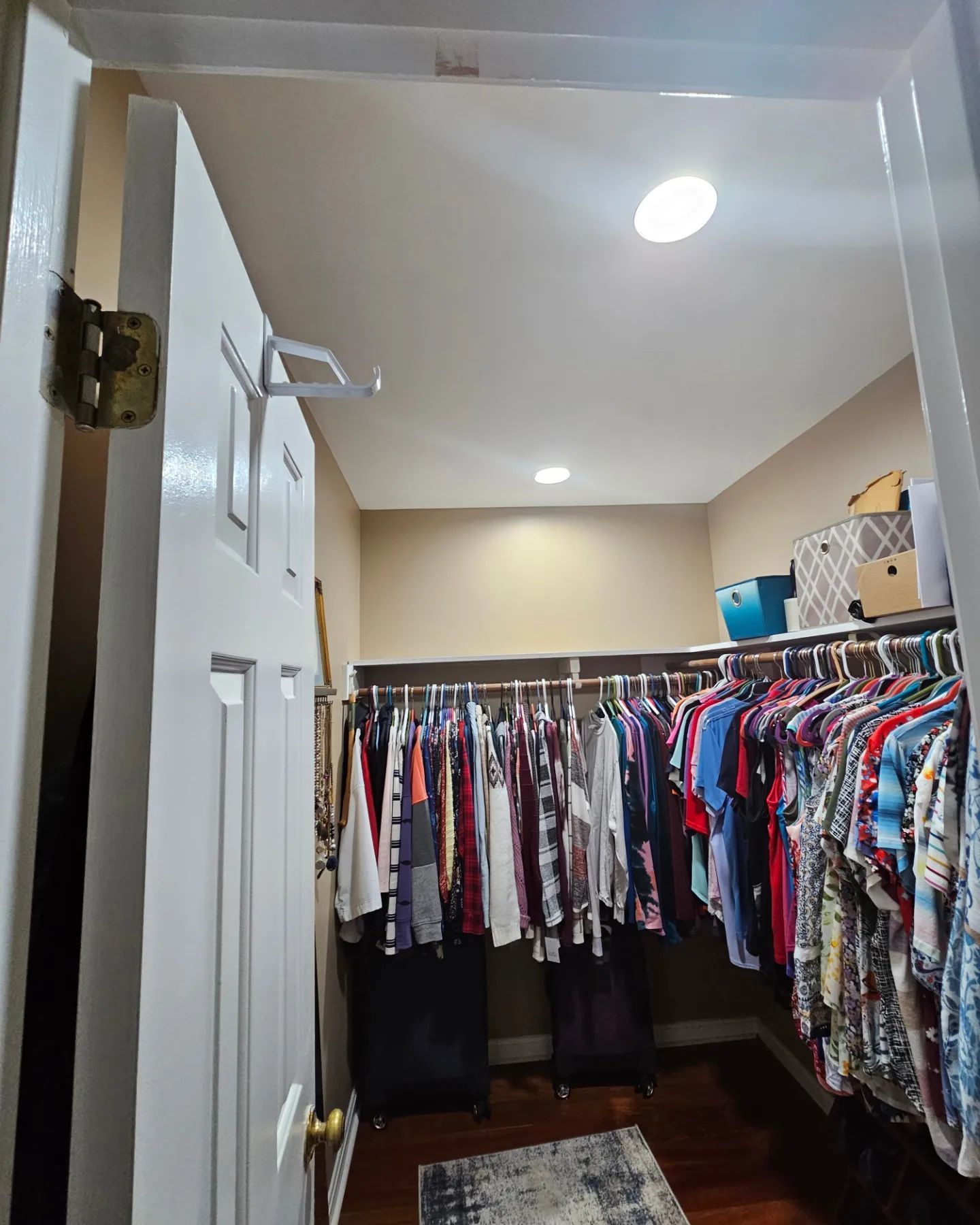 Open doorway to a narrow closet packed with hanging clothes and shelves, with a ceiling light overhead.