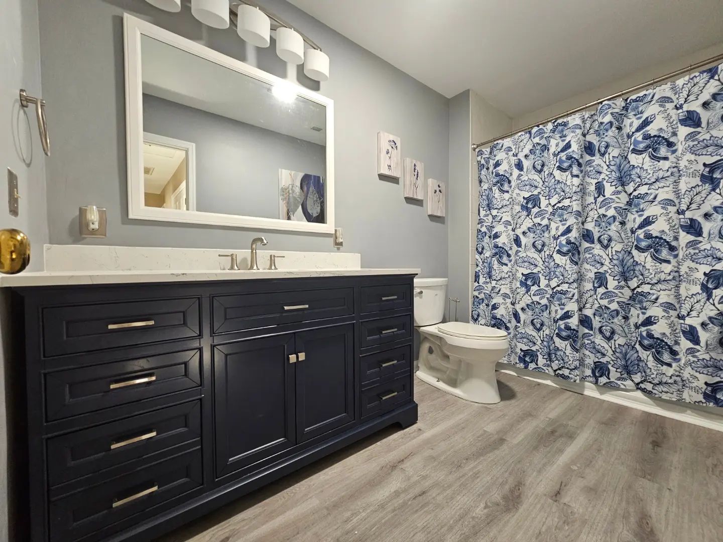 Modern bathroom with navy vanity, white sink and mirror, toilet, and blue floral shower curtain