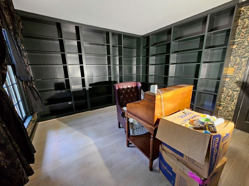 Empty room with dark built-in shelves, a wooden chair, and stacked boxes near the corner.