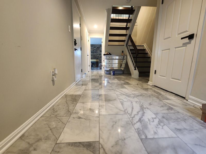 Marble-floored hallway with stairs, white doors, and a bright entryway at the far end
