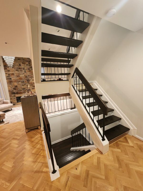 Modern stairwell with black open-riser stairs, white walls, and herringbone wood flooring.