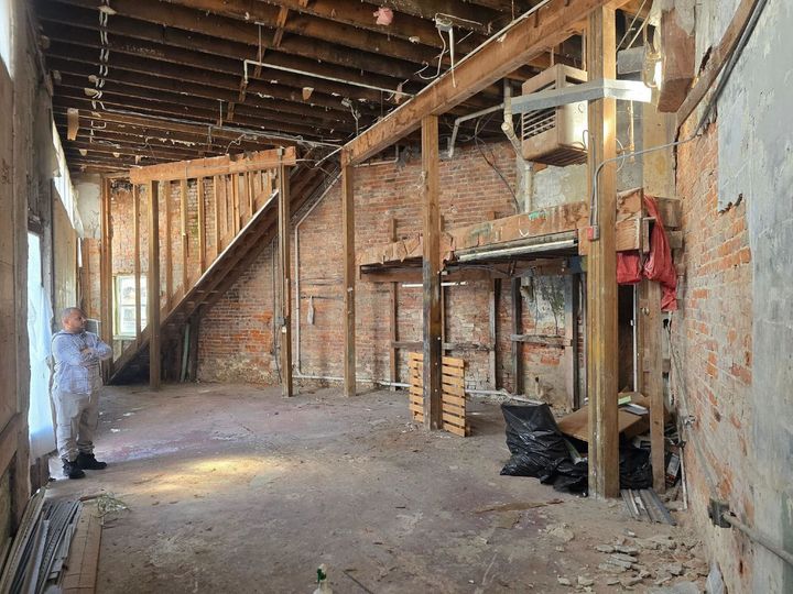 Empty unfinished room with exposed wooden framing, stairs, and construction debris on the floor