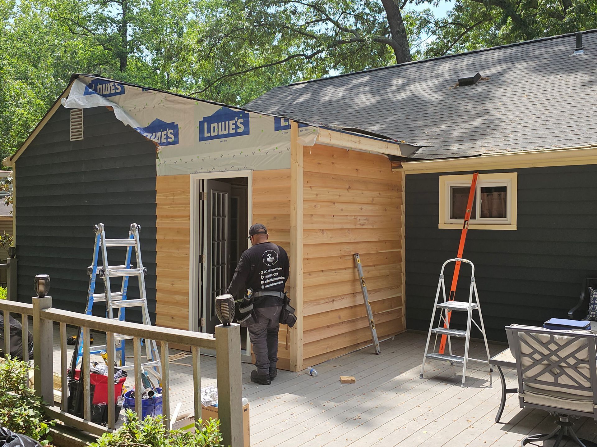 Workers installing wood siding on a dark house exterior with ladders and tools on a sunny day