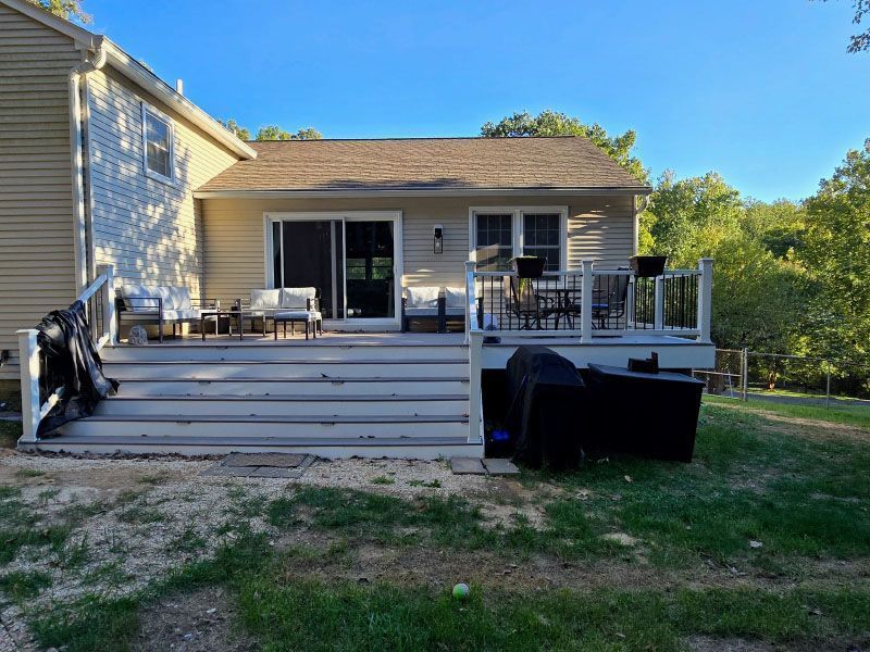 Backyard deck with gray railing, sliding glass doors, patio furniture, and a grill beside a house