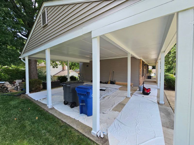 Covered porch with white columns, blue trash bins, and drop cloths during exterior house work