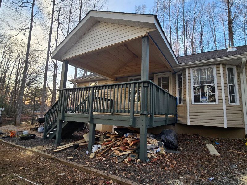 Covered porch addition on a house, with green railings and stairs amid construction debris.