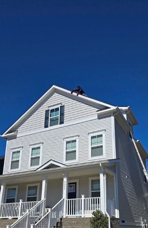 Worker on a roof of a white house under a clear blue sky