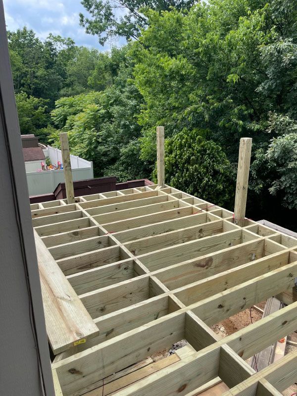 Framed wooden deck under construction beside a house, with trees in the background.