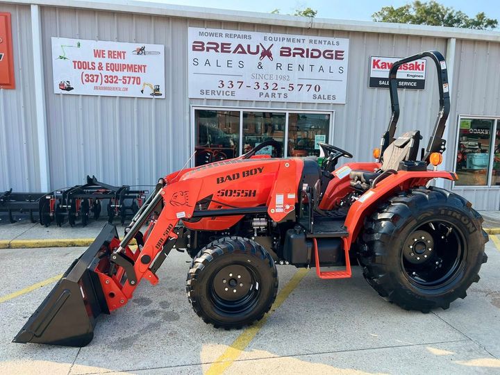 Orange front-end loader parked outside a tractor sales shop with “BREAK A BRIDGE” signage.