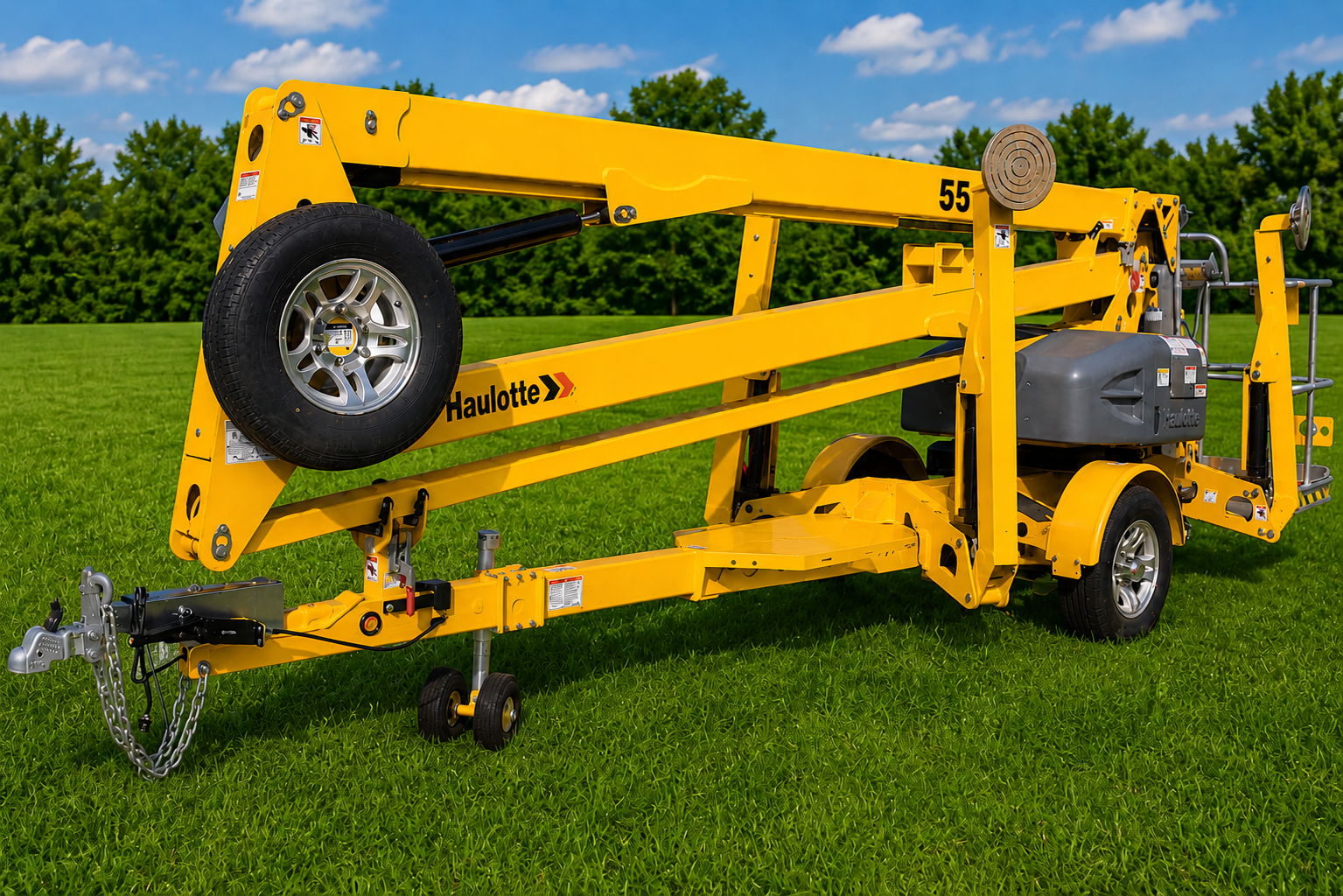 Yellow boom lift parked on grass under a blue sky, with its arm folded and wheels visible
