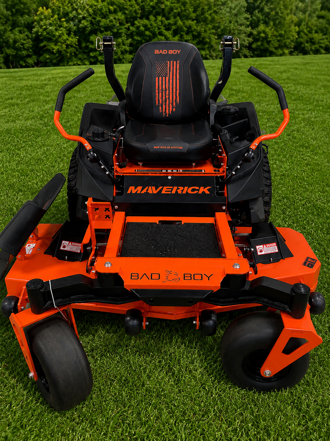 Orange and black riding lawn mower on grass with trees in the background