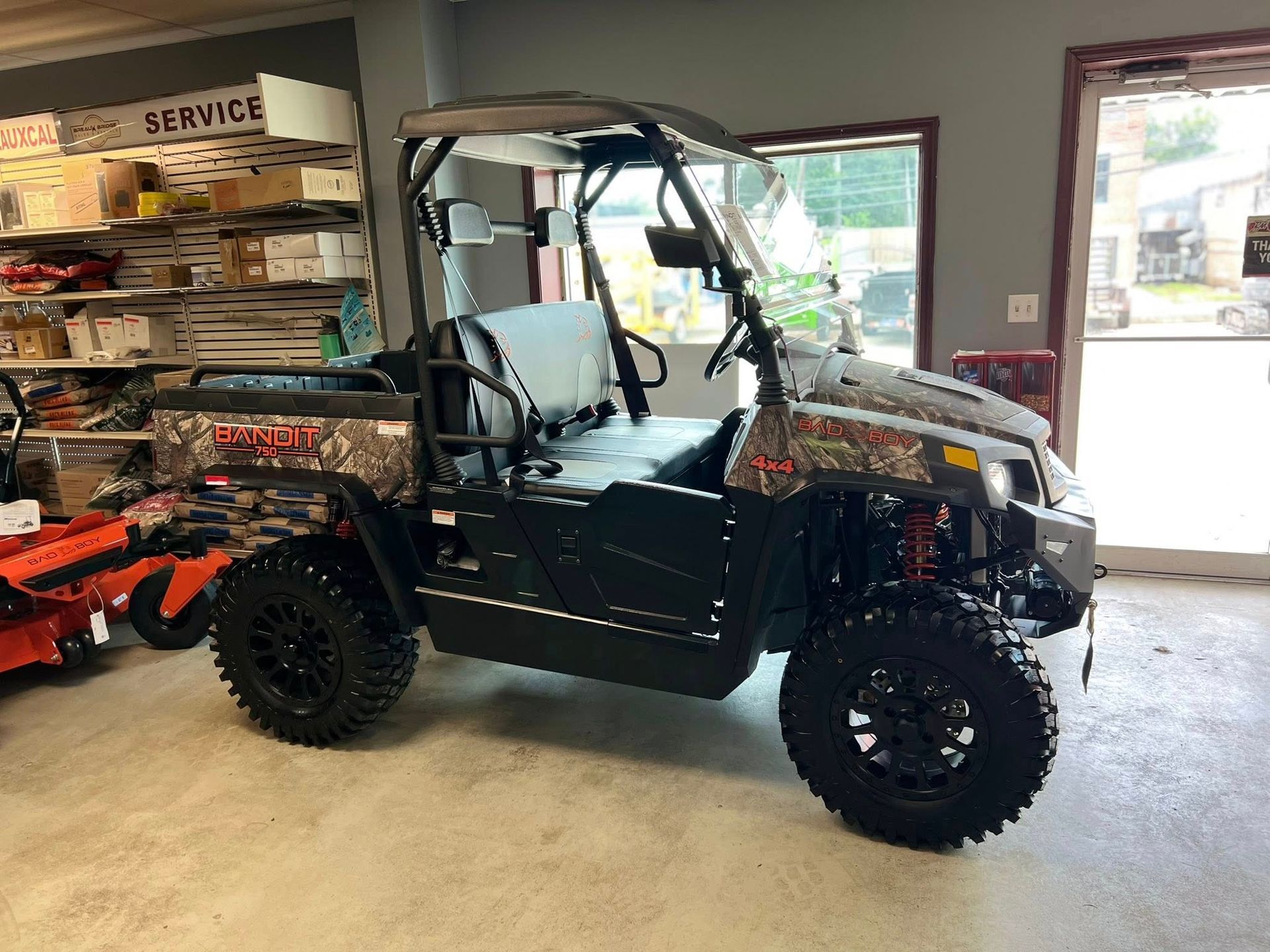 Black off-road UTV with camouflage roof parked inside a service shop near a doorway.