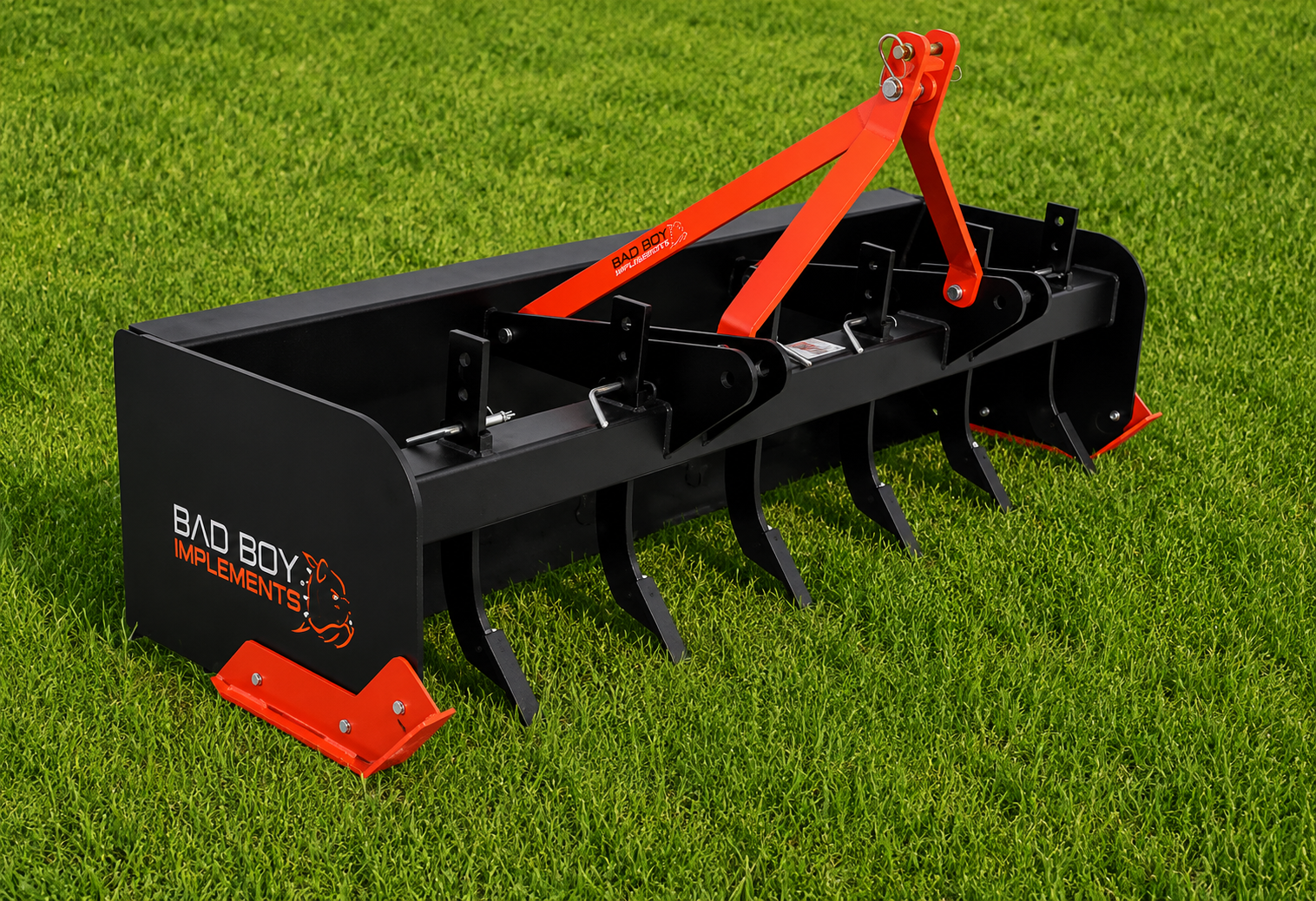 Black tractor attachment with red lift arms and tines sitting on grass