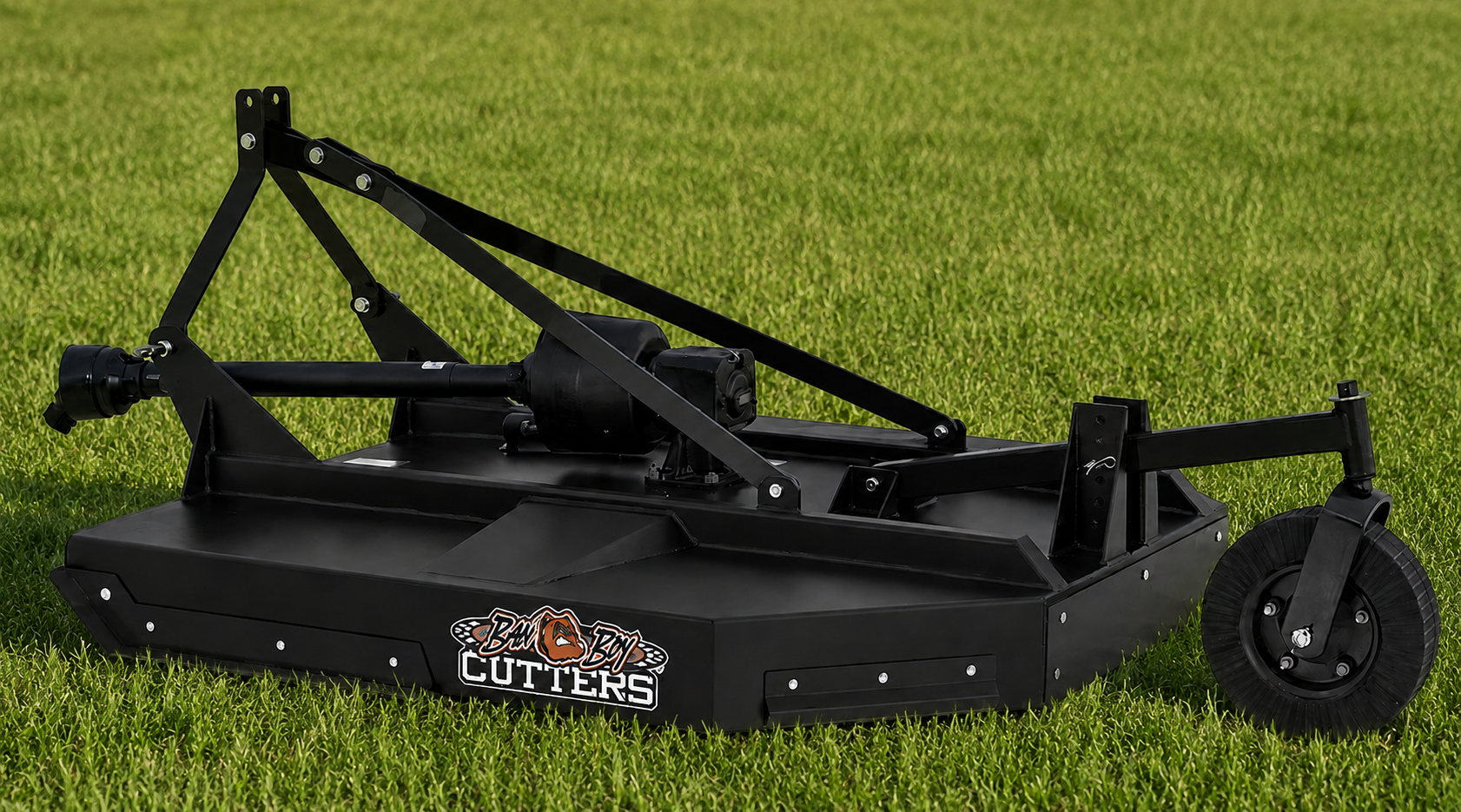 Black tow-behind lawn mower deck on grass, with large side wheels and exposed frame