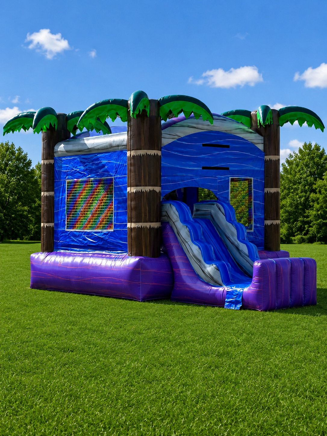 Blue inflatable palm-tree bounce house with slide on a grassy field under a sunny sky