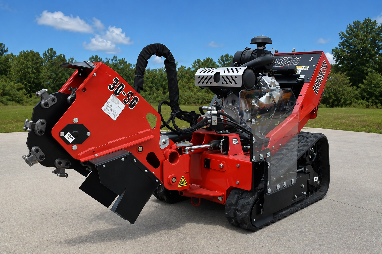Red compact tracked utility loader with attached auger on a paved lot, trees in the background
