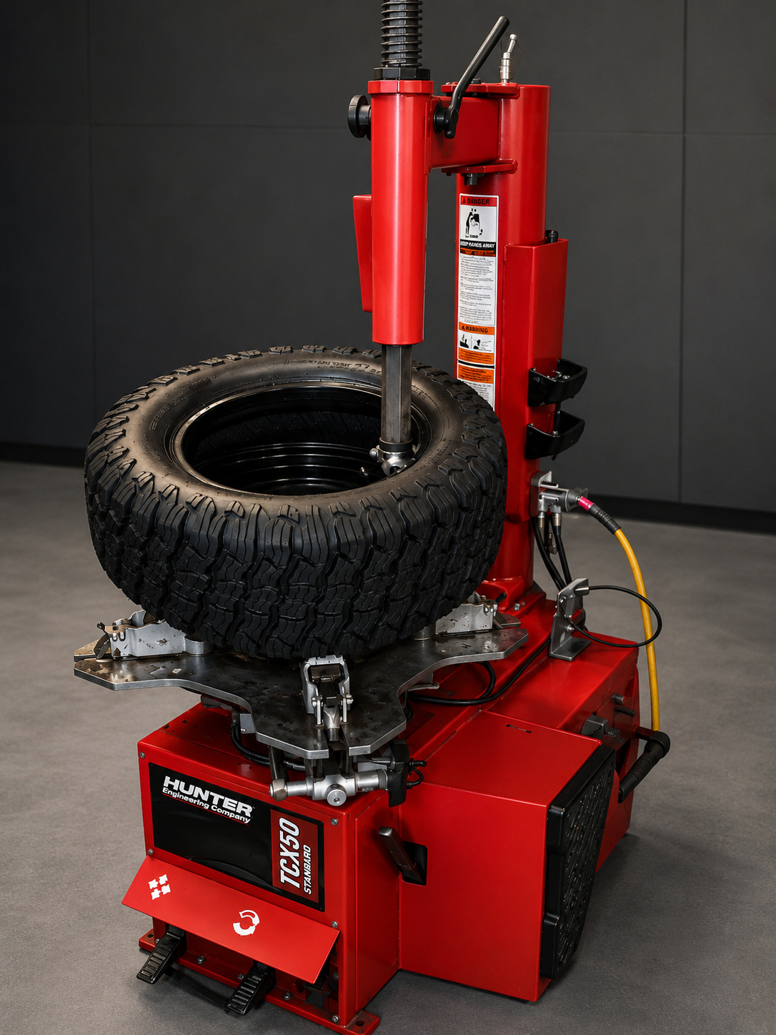 Red tire-changing machine with a tire mounted on its turntable in a workshop.