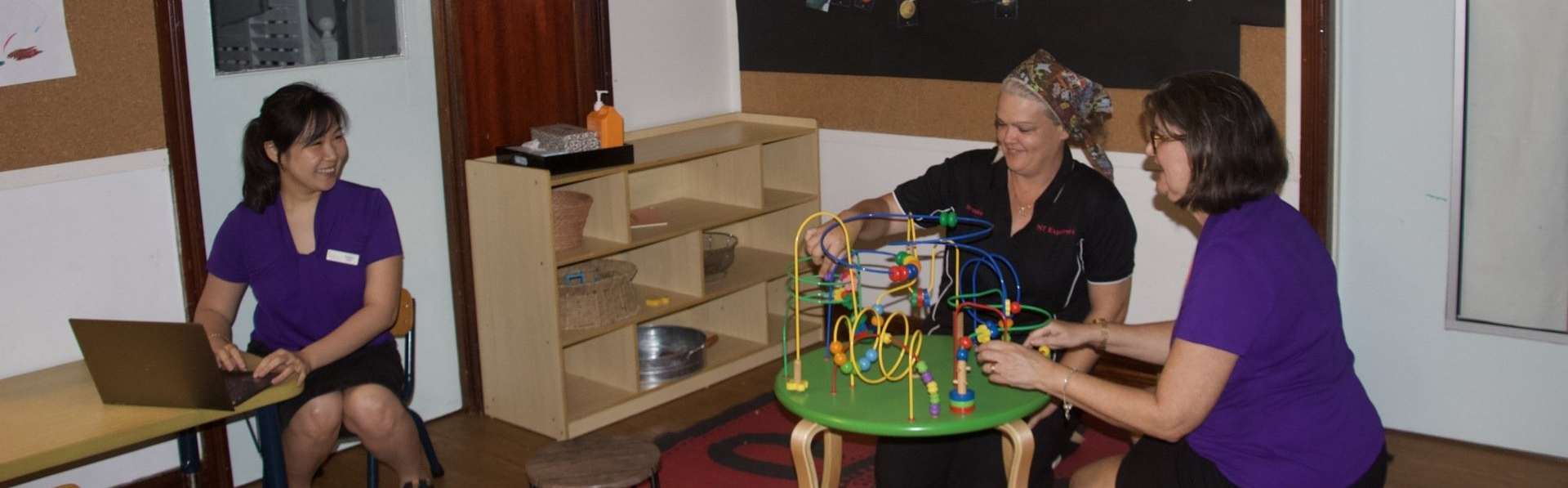 Three women are sitting around a green table playing with toys.