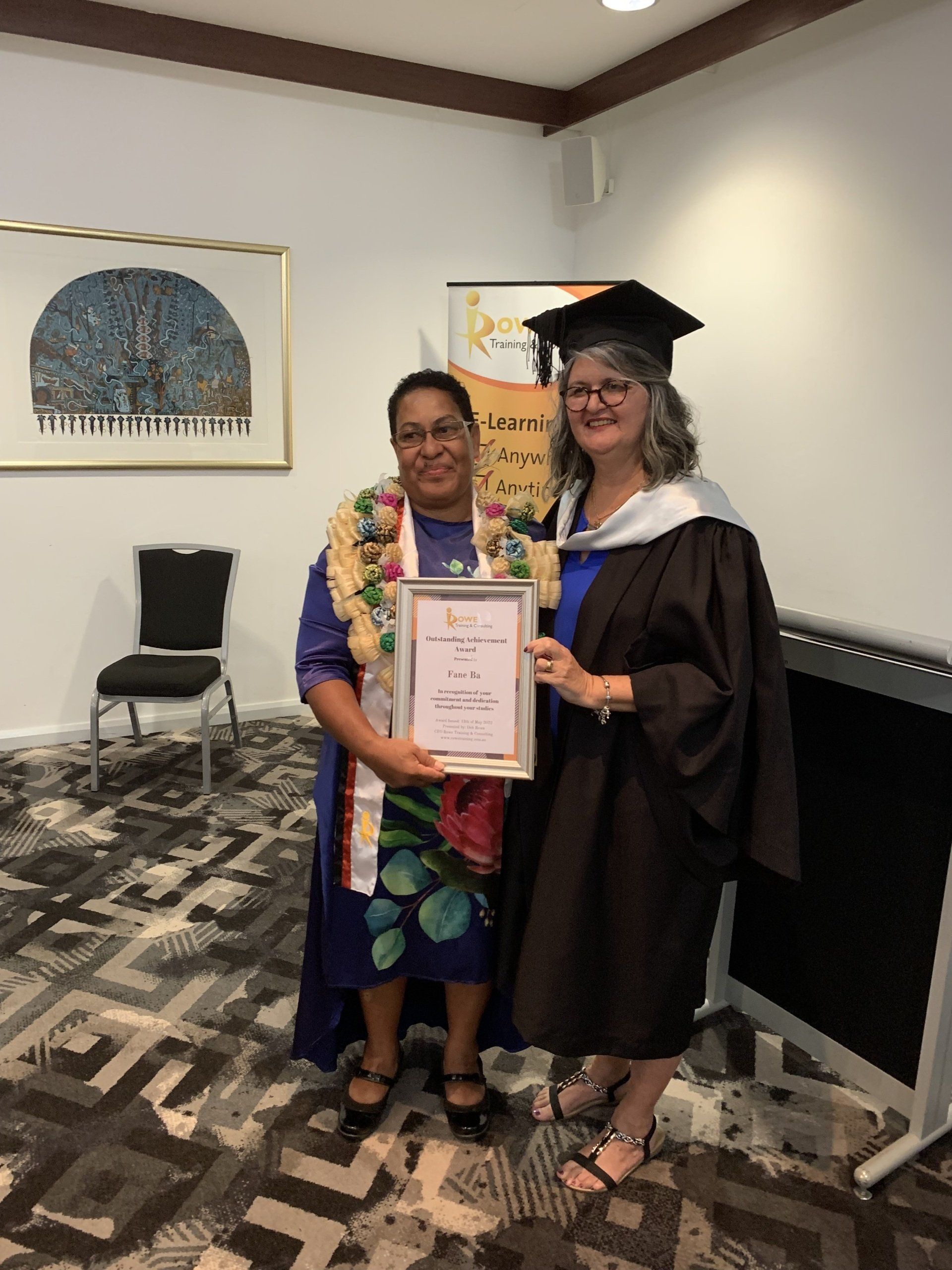 Two women in graduation gowns are standing next to each other holding a certificate.