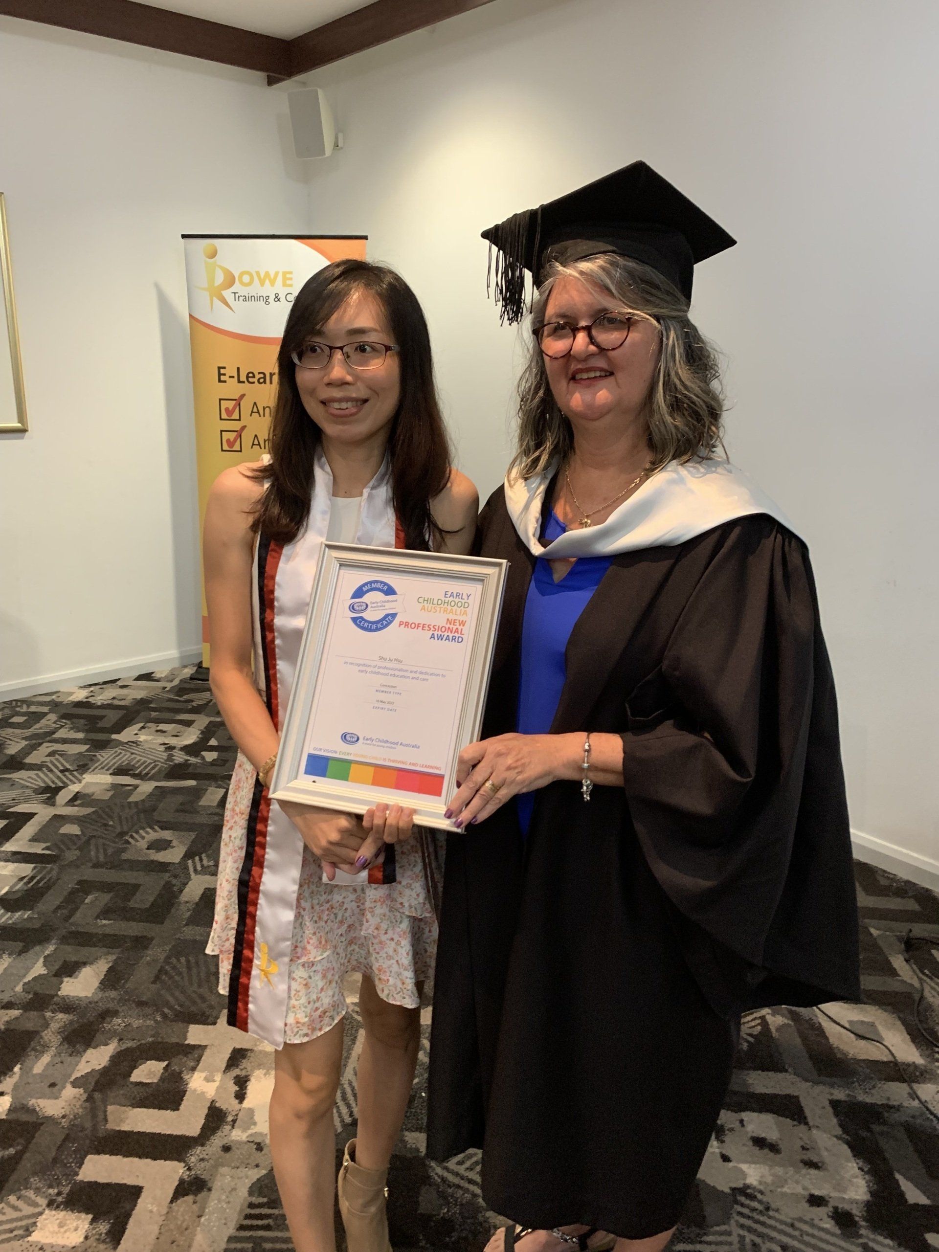 Two women in graduation gowns are standing next to each other holding a certificate.