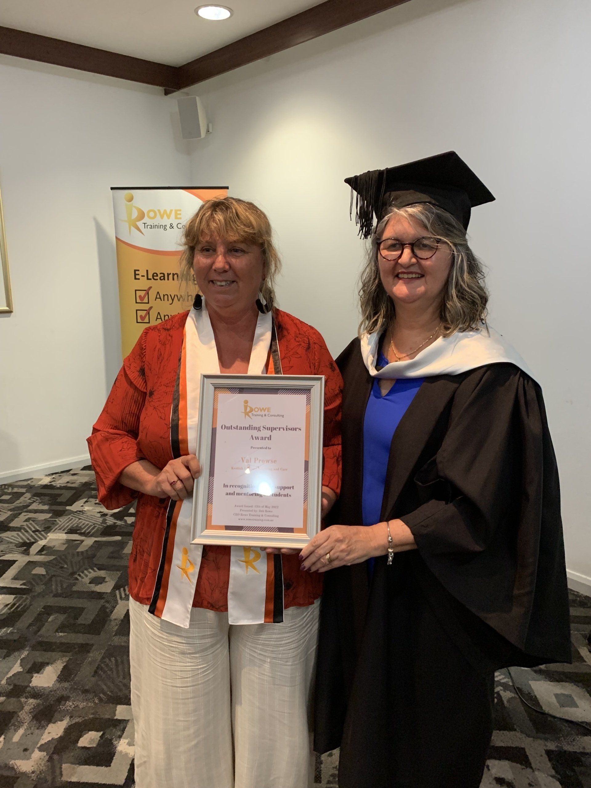 Two women in graduation gowns are standing next to each other holding a certificate.