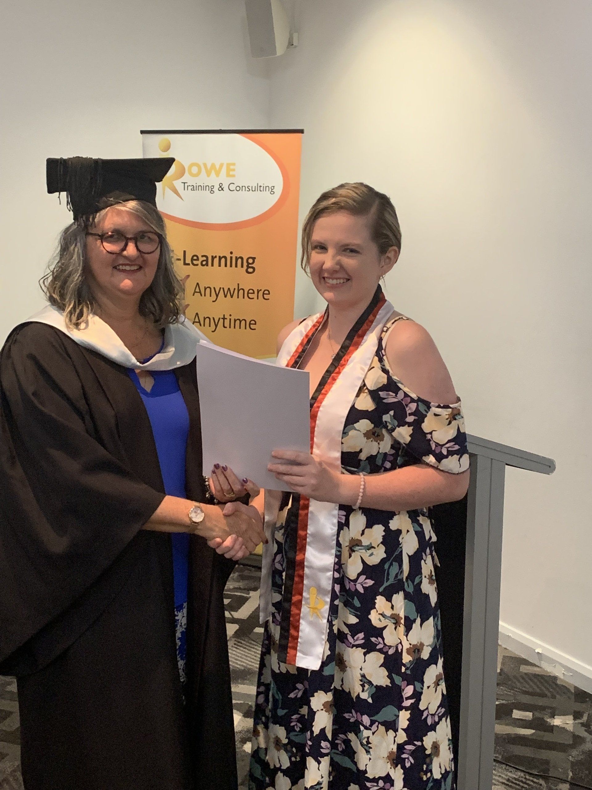A woman in a graduation cap and gown is shaking hands with another woman