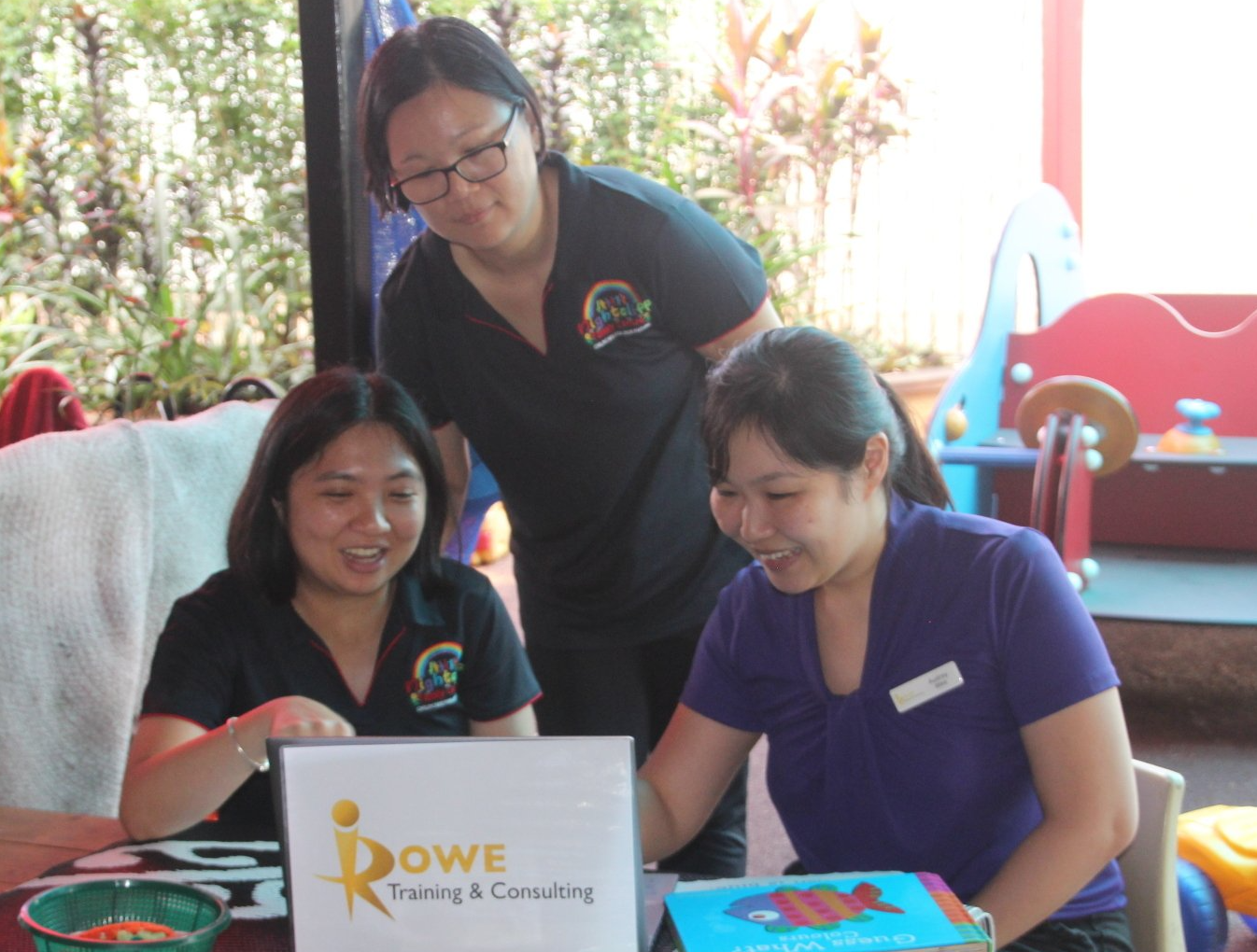 Three women looking at a sign that says rowe training & consulting