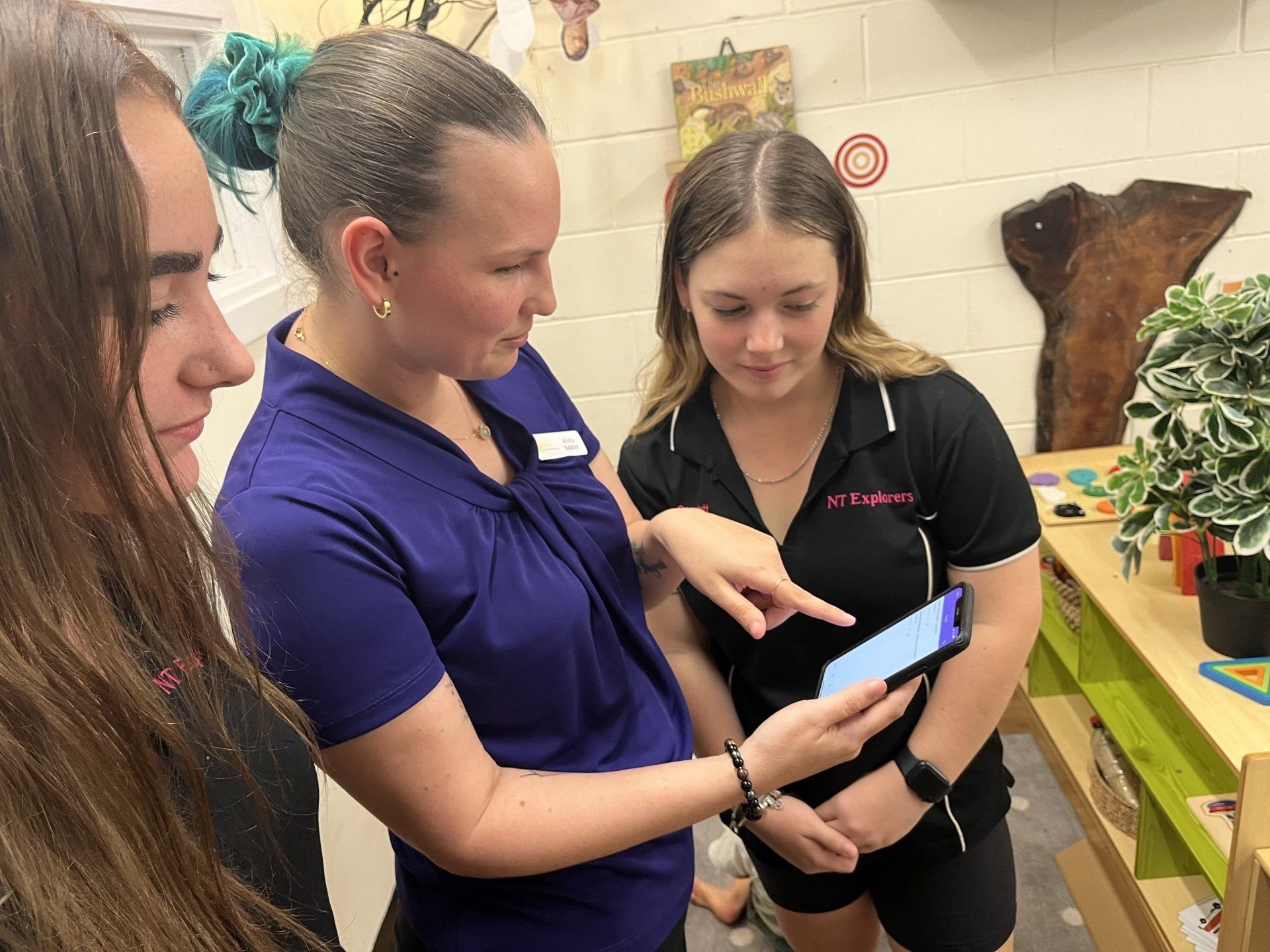 A group of young women are looking at a cell phone.