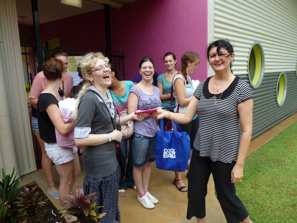 A group of women are standing outside of a building and one of them is holding a blue bag that says ' sydney '