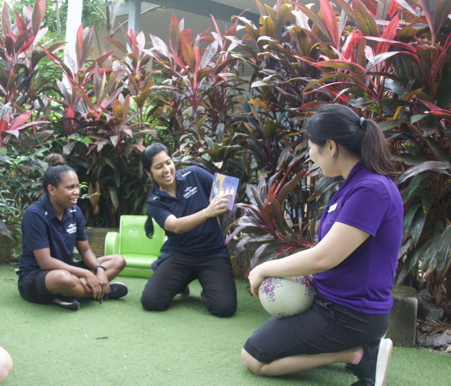 A woman in a purple shirt is kneeling down with a soccer ball