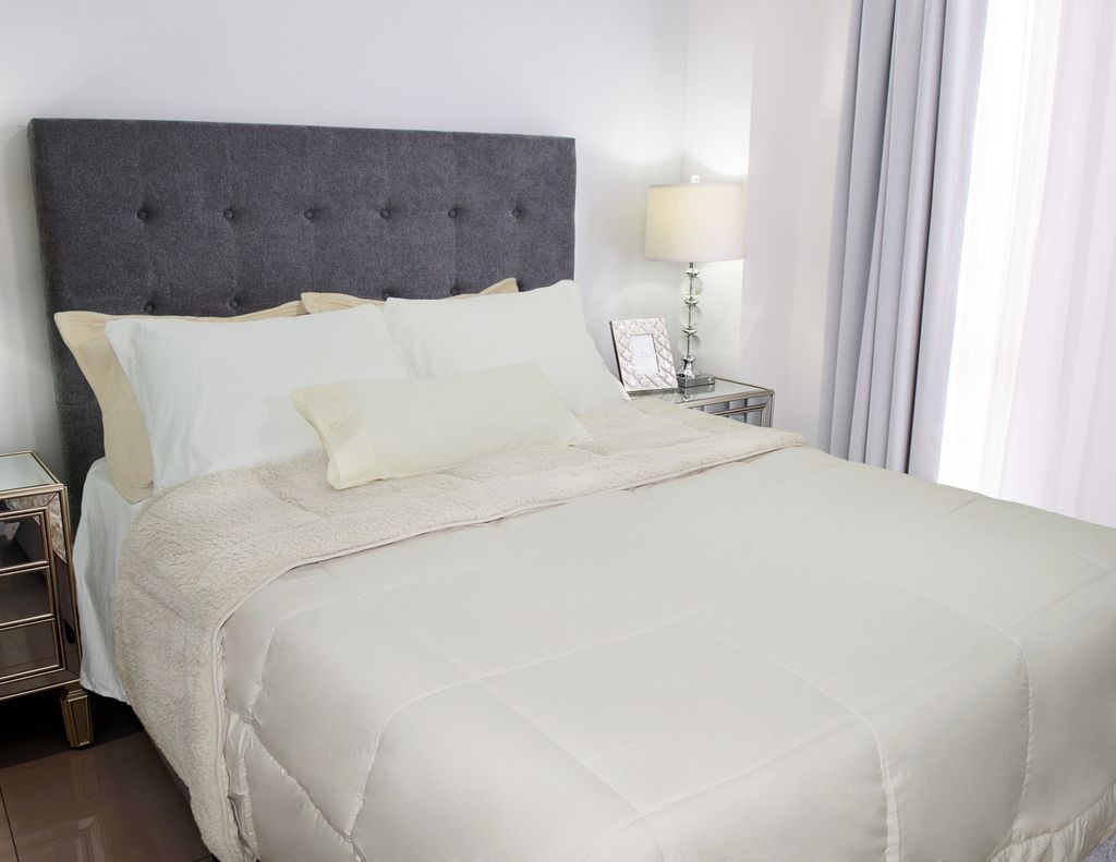 Una cama con cabecero tapizado en gris y ropa de cama blanca, junto a una mesita de noche.