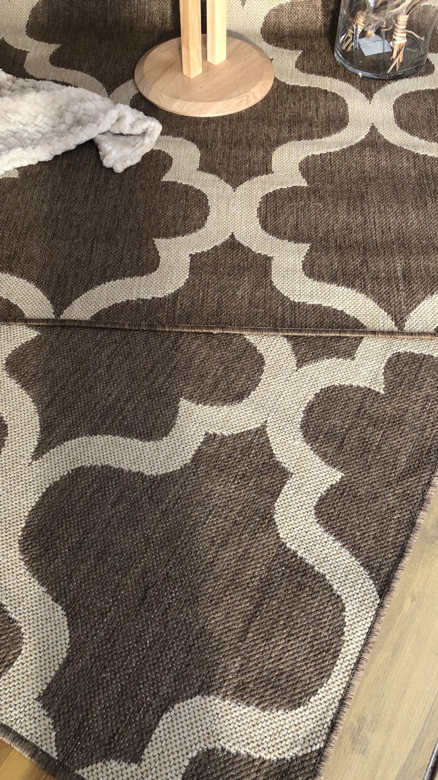 Alfombra estampada en tonos marrones y blancos con base de madera y jarrón de cristal encima.