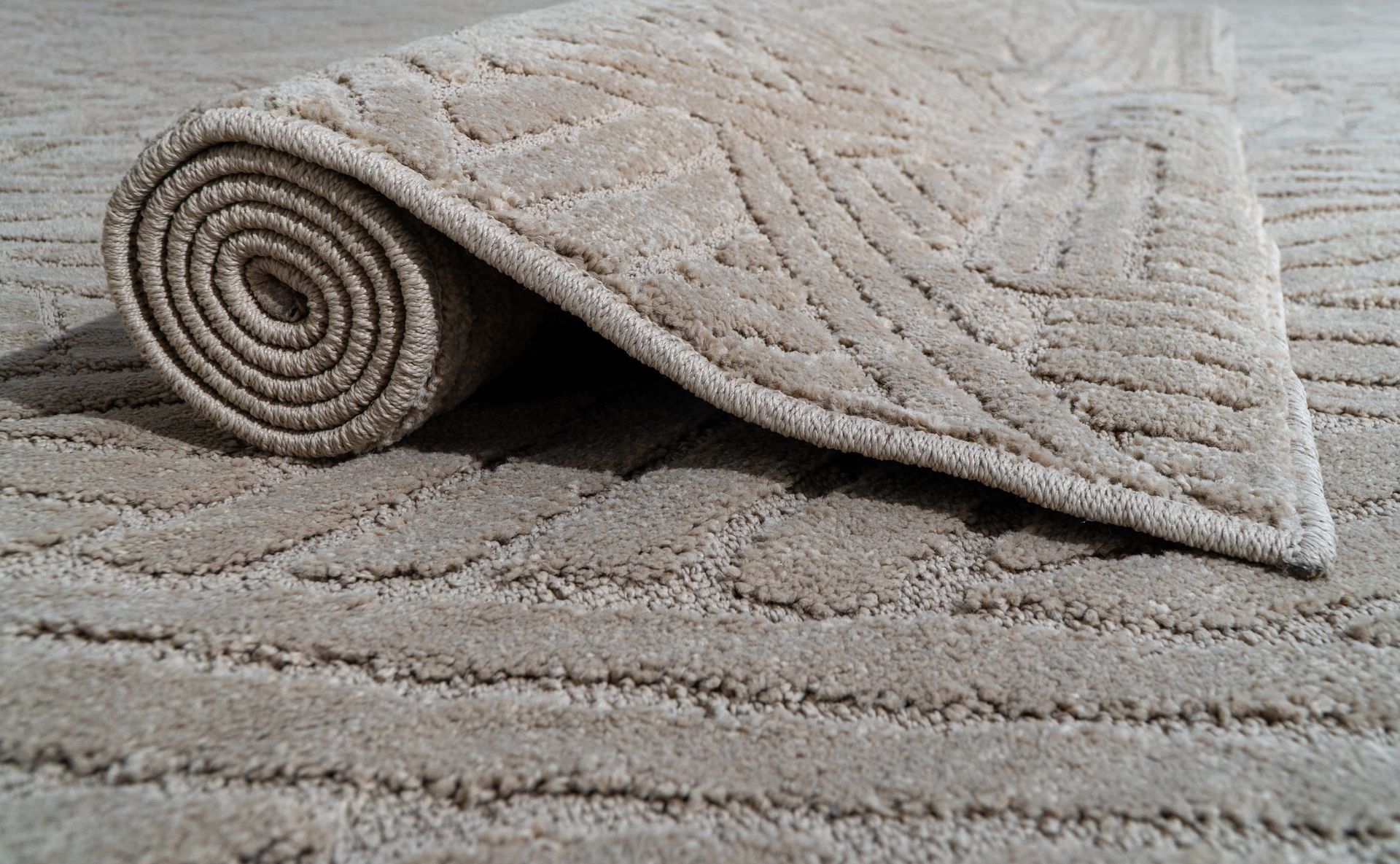 Alfombra beige estampada, parcialmente enrollada, dejando al descubierto la parte inferior.