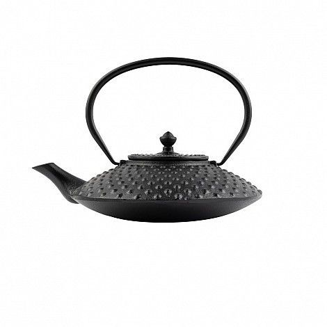Tetera de hierro fundido negro con superficie tachonada, pico y asa sobre fondo blanco.