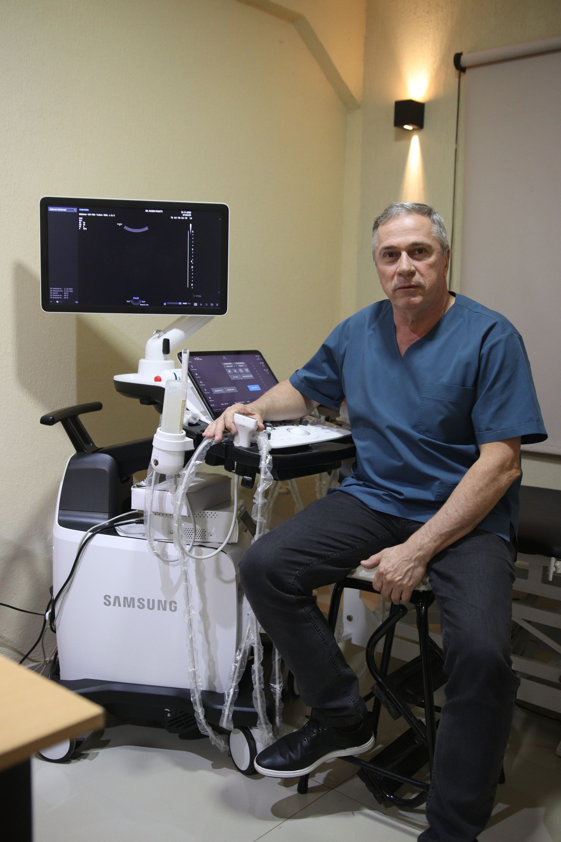 Hombre sentado junto a una máquina de ultrasonido médico en una sala clínica.