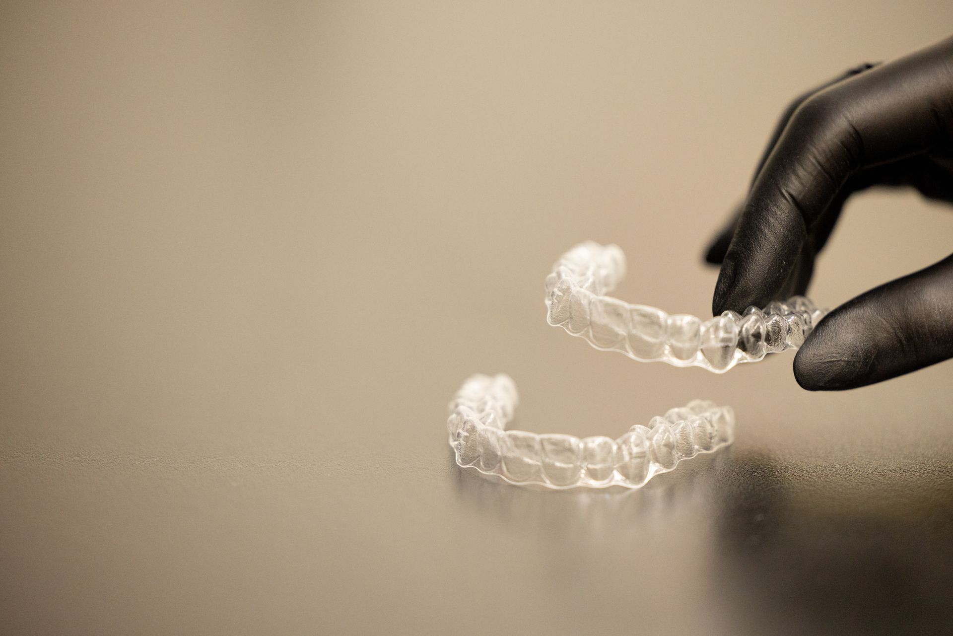 Gloved hand holding clear dental aligners on a beige background Gloved hand holding clear dental aligners on a beige background