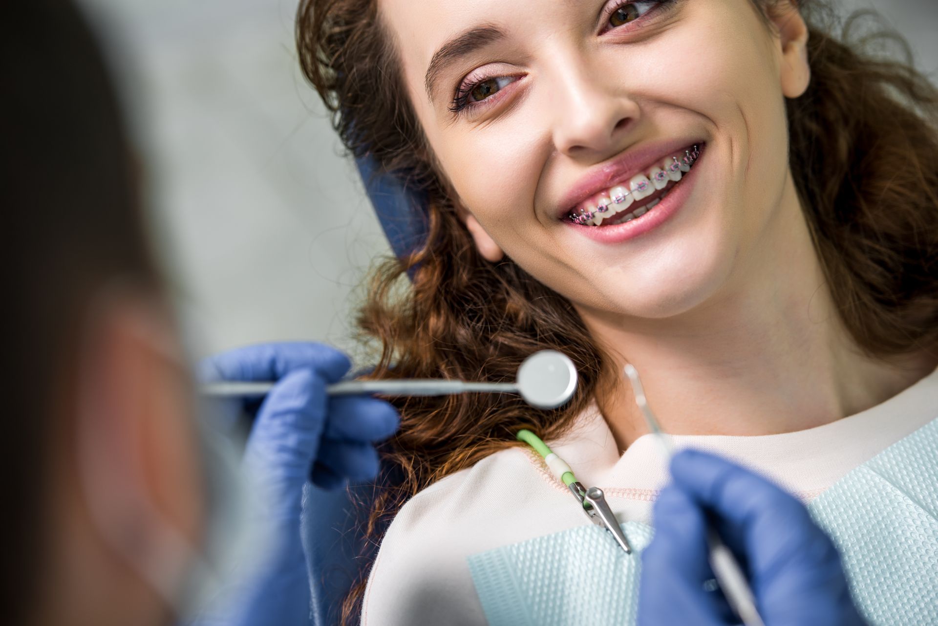 Dentist examining a smiling patient’s teeth with a dental mirror and gloves