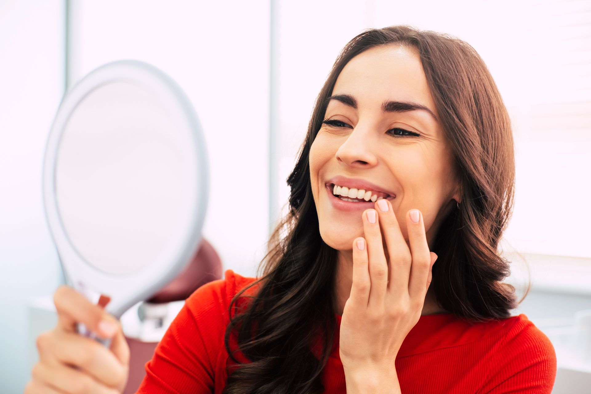 Smiling woman touching her cheek while looking in a mirror, in a bright room