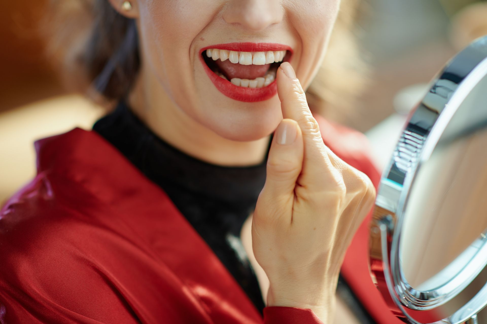 Woman applying red lipstick while looking into a handheld mirror
