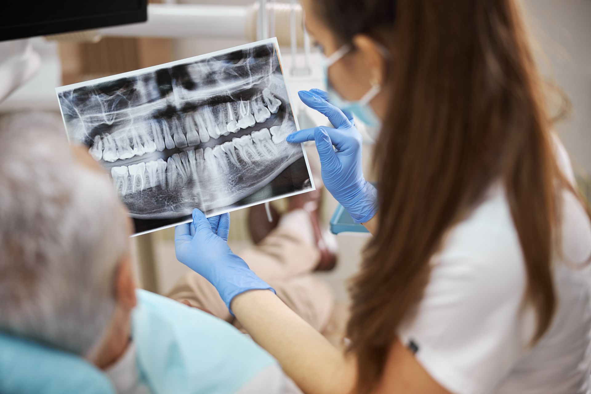 Dentist in blue gloves shows dental X-rays to a seated patient in a clinic