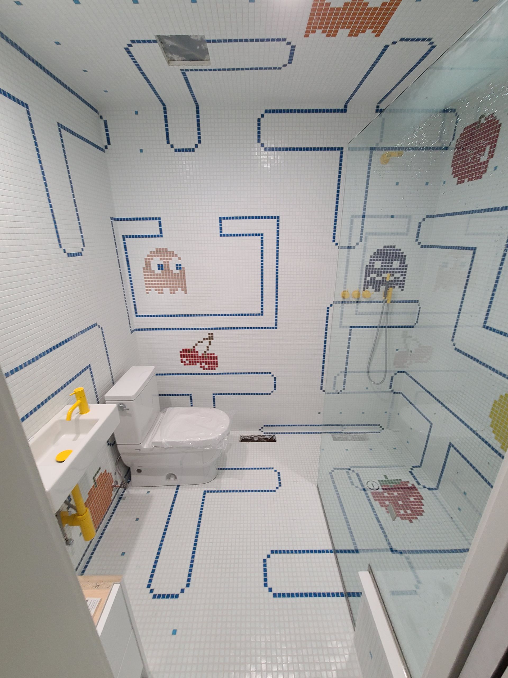 A bathroom with a toilet , sink , shower and a maze on the wall.