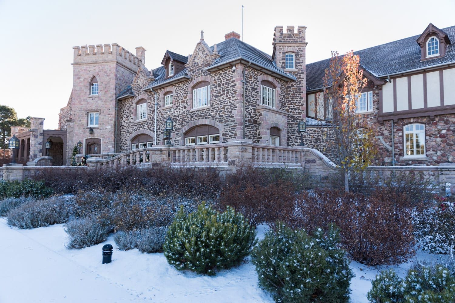 Stone castle with snow-covered bushes in foreground.