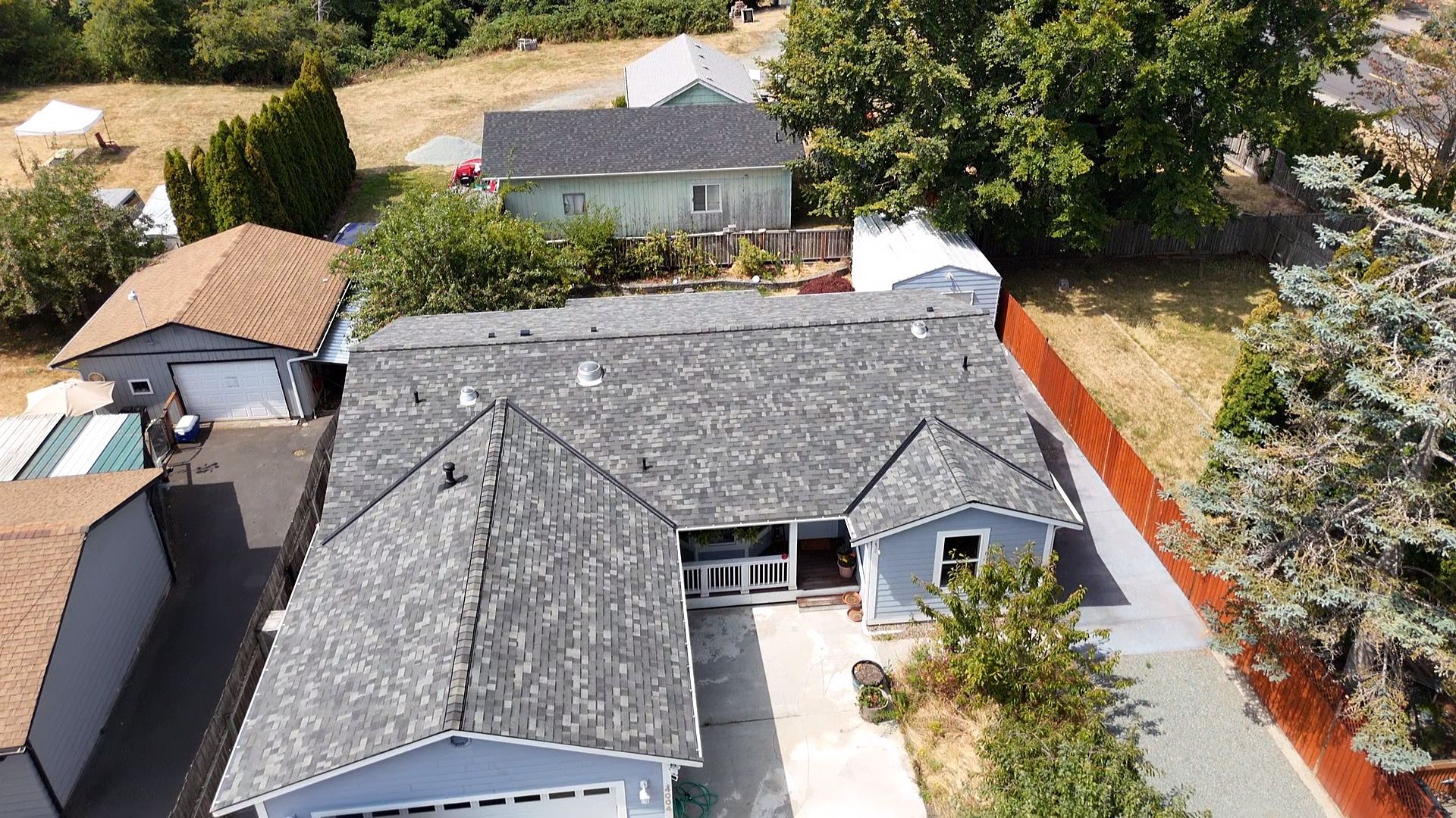 Aerial view of a suburban house with a gray roof, front yard, and neighboring homes.