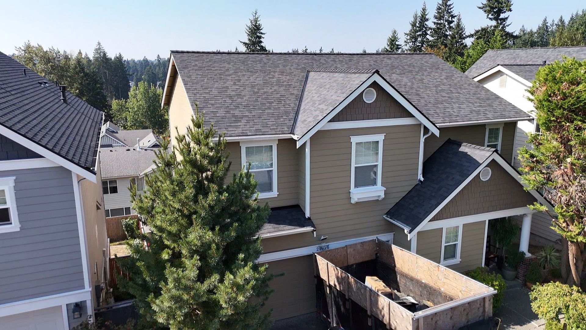 Suburban house with tan siding and gray roof, seen from above with trees and neighboring homes nearby