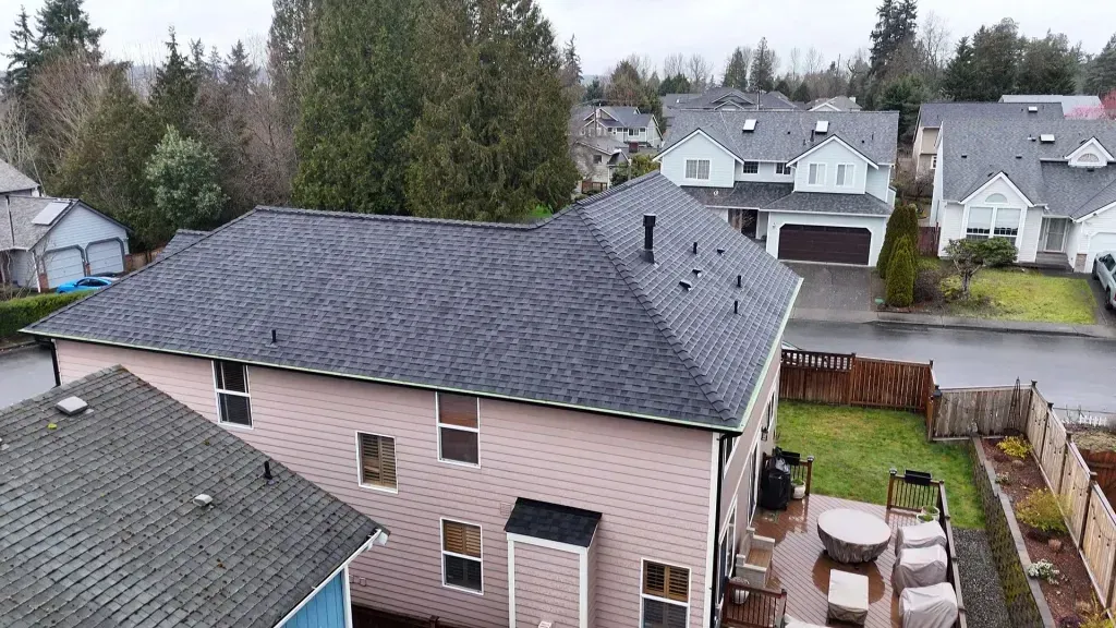 Backyard view of a gray-roofed house with neighboring homes and trees beyond the fence