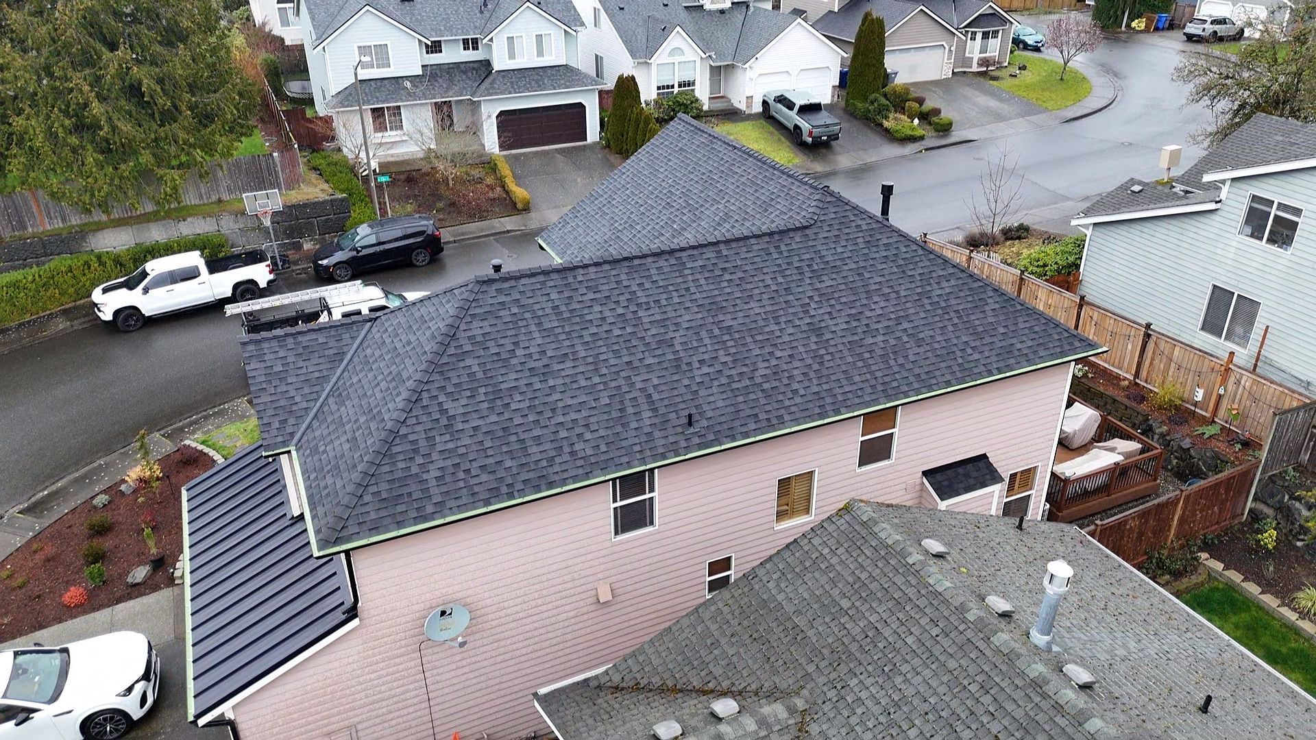 Aerial view of a suburban house with a dark roof and pink siding on a wet residential street.