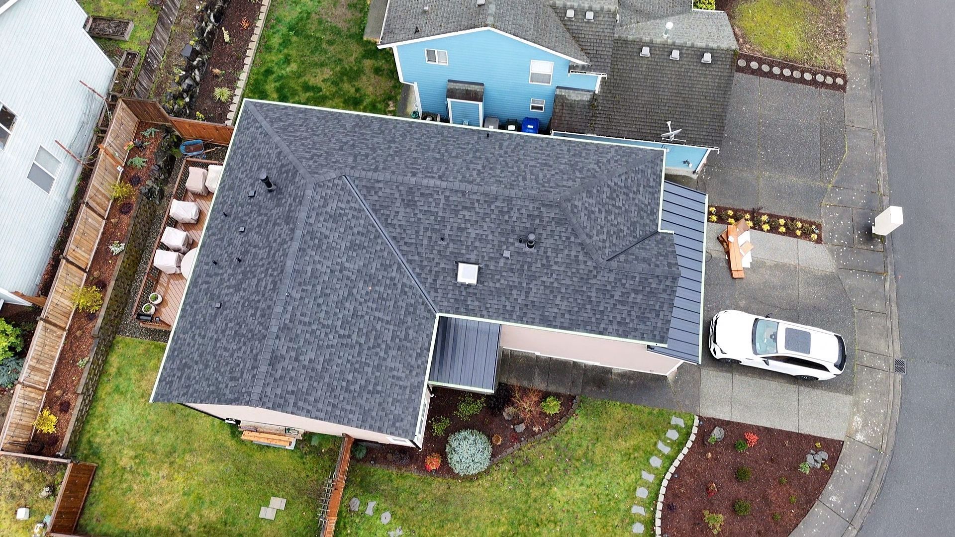 Aerial view of a house with a dark roof, driveway, parked white car, and neighboring homes.