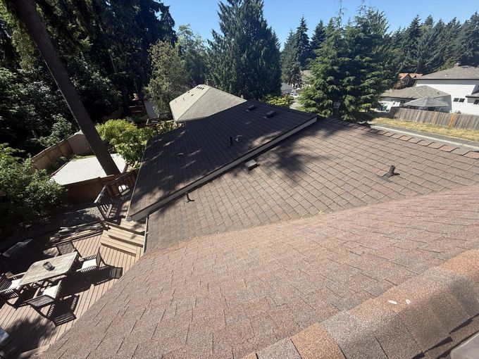 Roof covered in brown shingles with trees and houses in the background