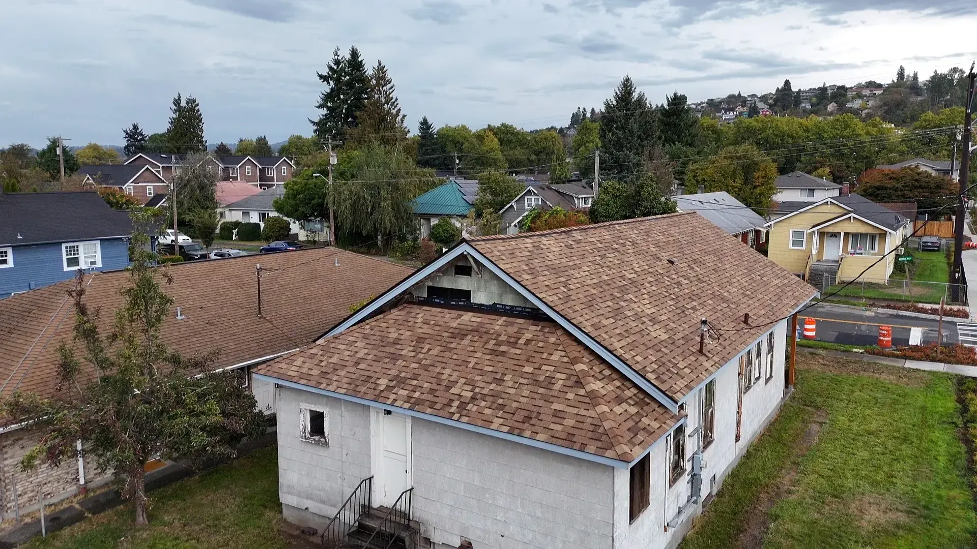 Aerial view of a white house with a brown roof in a suburban neighborhood, with trees and hills in the background
